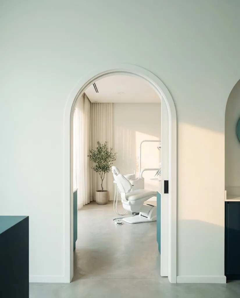 Arco blanco que enmarca un consultorio dental luminoso con sillón blanco y olivo